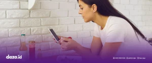 seorang wanita berbaju putih sedang memegang hp. Scrolling aplikasi pemesanan online terbaik