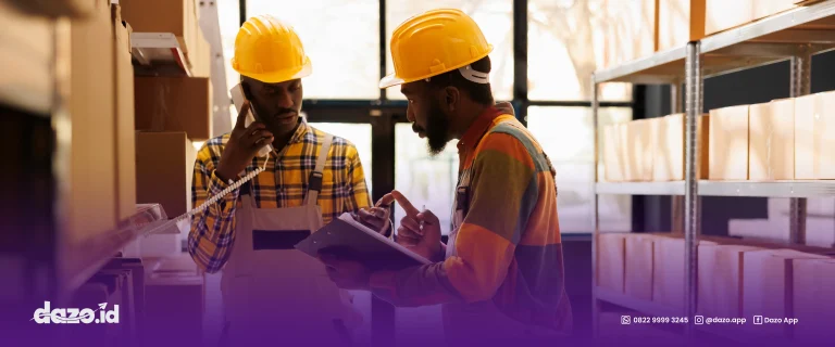 dua orang karyawan menggunakan helm proyek berwarna kuning sedang berbincang, yang satu sedang berbicara di telepon yang satunya lagi sedang membawa tablet membicarakan supply chain management