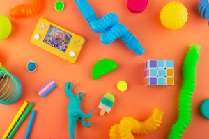 Terdapat beberapa pilihan produk mainan anak yang terpampang seperti mainan dinosaurus berwarna biru, bola berwarna kuning, rubik, dan pensil warna